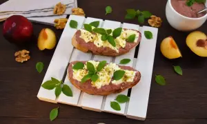 Zwei Bruschettas mit Pflaumenaufstrich, Käse und Basilikum, garniert mit Walnüssen und frischen Pflaumen.