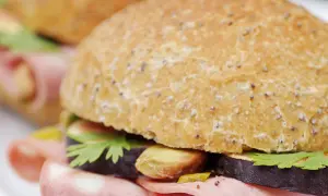 Un délicieux sandwich mortadelle garni de tranches d'aubergine, de pistaches et de persil frais, prêt à être dégusté.