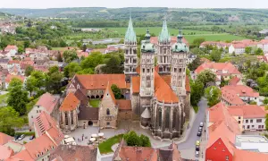 Der Naumburger Dom, ein Meisterwerk romanischer Architektur, thront über der Stadt. Seine Türme ragen in den Himmel, umgeben von roten Dächern und grünen Hügeln.
