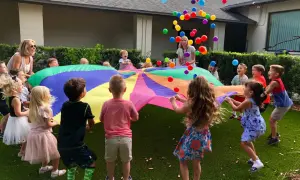 Children joyfully engage in gross motor activities for toddlers, tossing colorful balloons into the air while holding a large parachute.