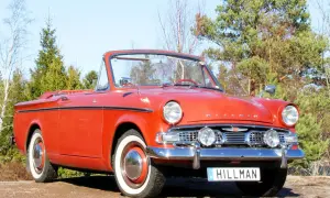 En röd cabriolet, en klassisk Hillman bil, står parkerad utomhus bland träd.