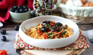 En skål med spaghetti puttanesca, toppad med svarta oliver och persilja. Ett härligt recept för en smakrik middag.