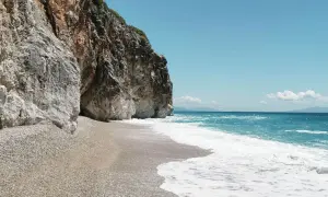 Skaliste klify otaczają kamienistą plażę Gjipe Beach, gdzie turkusowe morze łagodnie faluje.