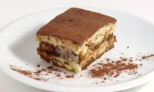 Une part de tiramisu, avec sa traduction française, est saupoudrée de cacao sur une assiette blanche.