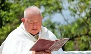 Kapłan w białej szacie zamyślony nad księgą, w jego oczach widać żal za grzechy.