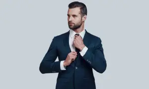 Elegancki mężczyzna w granatowym garniturze poprawia krawat. Idealna biała koszula do granatowego garnituru.
