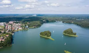 Malownicze pojezierza w Polsce: zielone wyspy na spokojnej tafli jeziora, miasteczko i żaglówki pod błękitnym niebem.