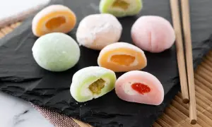 Kolorowe ciasteczka mochi z owocowym nadzieniem, ułożone na czarnej desce, obok pałeczek.