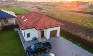 Nowy dom z garażem i dwoma samochodami na podjeździe. W tle pola i inne zabudowania. To miejsce idealne na darowiznę udziału w nieruchomości wspólnej.