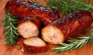 Pyszna, rumiana kiełbasa z piekarnika, skropiona sokami, z gałązkami rozmarynu i ziarnami pieprzu.