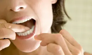 Kobieta pokazuje, jak używać nici dentystycznej, czyszcząc zęby.
