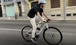 Un joven con casco y ropa casual pedalea una bicicleta eléctrica por la ciudad.