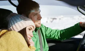Ett par i en vinter bil, hon med mössa och gul tröja, han kör i grönt.