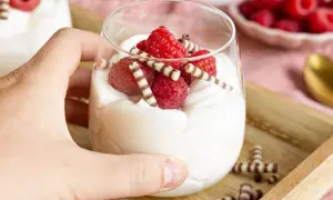 Ein Glas mit cremigem Quark-Dessert, garniert mit frischen Himbeeren und Schokoröllchen.