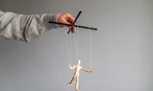 Dłoń w szarym swetrze steruje drewnianą marionetką. To obraz manipulatora, który pokazuje swoje cechy.