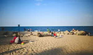 Ludzie odpoczywają na plaży nad morzem. Choć Szczecin nie leży bezpośrednio nad morzem, jego bliskość jest odczuwalna.