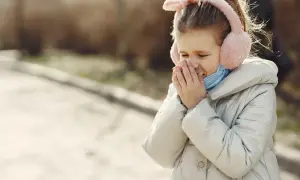 Lindra hosta barn: Flickan med fluffiga hörselkåpor hostar och håller handen för munnen, kanske behöver hon hostmedicin.