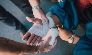 Mains bandant une blessure, peut-être suite à une violence involontaire. L'une des mains est bandée, l'autre tient la compresse.