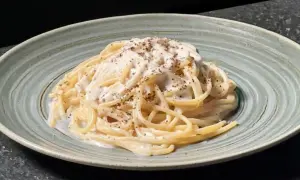 Un plat de tonnarelli cacio e pepe crémeux, saupoudré de poivre noir fraîchement moulu, servi dans une assiette texturée.