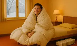 Uomo avvolto in una coperta, sorride mentre fuori nevica. Un termosifone è visibile, suggerendo la lotta contro la dispersione termica in casa.