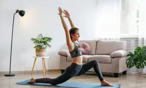 Une femme souriante pratique le yoga à la maison, profitant des bienfaits de cette discipline pour son bien-être.