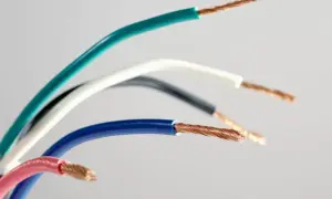 Różne **kolory faz** kabli elektrycznych: zielony, biały, szary, niebieski i różowy, z odsłoniętymi miedzianymi żyłami.