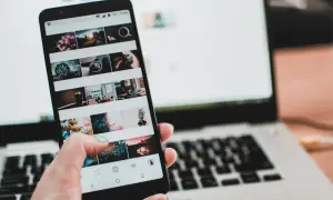 Dłoń trzyma smartfon z widokiem na ekran z siatką zdjęć. Obok leży laptop. Czy to połączenie przez miracast?