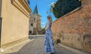 Kobieta w kwiecistej sukience podziwia biecz atrakcje: zamek i brukowaną uliczkę.
