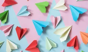 Kolorowe papierowe samolociki, jak się robi origami. Różne odcienie papieru ułożone na tle geometrycznych kształtów.
