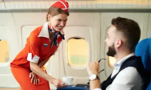 Uśmiechnięty stewardesa w pomarańczowym stroju podaje kawę pasażerowi w samolocie.