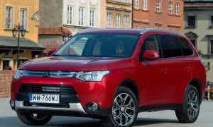 Czerwony Mitsubishi Outlander na tle kamienic. Wiele osób szuka mitsubishi outlander opinie, by podjąć decyzję o zakupie.