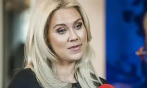 Caroline Hainer, med blont hår och makeup, ser åt sidan. En mikrofon syns i förgrunden.