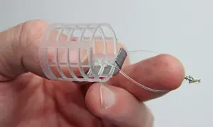 Ein Finger hält einen selbstgebauten Futterkorb mit Blei und Schnur.