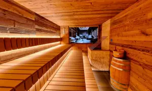 Gemütliche Holzsauna mit beleuchteten Bänken und einem Bild von einer Brauerei an der Wand. Ein Bierfass und ein Holzeimer stehen bereit für ein entspannendes Bier-Spa-Erlebnis.