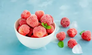 En skål med frostiga jordgubbar, redo att frysa in för framtida användning. Några jordgubbar och isbitar ligger utspridda bredvid.