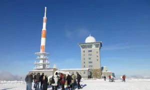 Menschen stehen im Schnee vor dem Brocken-Wetterturm und dem Fernsehturm. Ein sonniger Tag im Winter auf dem Brocken.