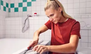 Frau entfernt mit einem Cuttermesser alte Silikonfugen an der Badewanne.