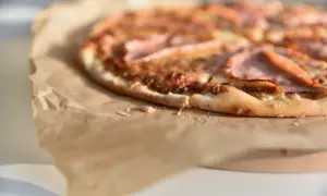 Zbliżenie na pizzę z szynką na papierze do pieczenia.