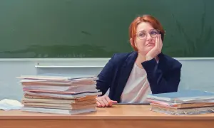 Nauczycielka zamyślona przy biurku, stosy papierów obok. Czy doczekamy się podwyżki dla nauczycieli? Najnowsze wiadomości.