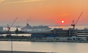 Sonnenuntergang im Hafen. Ein großes Kreuzfahrtschiff liegt vor Anker, während Kräne und Gebäude der port agency im warmen Licht erstrahlen.