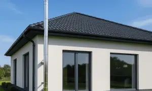 Nowoczesny dom z białym tynkiem, czarnym dachem i oknami. Na zewnątrz widoczna budowa komina systemowego ze stali nierdzewnej.
