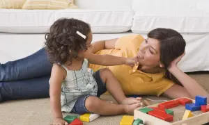 Mama uczy córkę, jak wychować dziecko, bawiąc się klockami na dywanie.