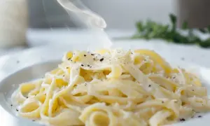 En ångande portion pasta alfredo, generöst toppad med riven parmesan och svartpeppar. Enkel men lyxig.
