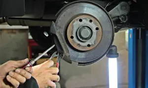 Mechanik wymienia linkę hamulca ręcznego, używając narzędzi do demontażu zacisku hamulcowego przy tarczy.