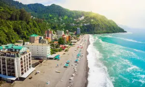 Widok na wybrzeże Gruzji, gdzie zielone wzgórza schodzą do piaszczystej plaży i turkusowego morza. Widać hotele i turystów odpoczywających nad wodą.