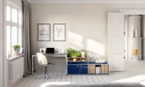 Accogliente stanza studio piccola con scrivania, piante e un'antica stufa in maiolica visibile attraverso una porta aperta.