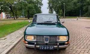 En grön Saab 99 står parkerad på en tegelstensbelagd uppfart, redo för en tur genom svenska landskap.