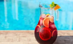 Pichet de sangria recette, rempli de fruits et de glaçons, prêt à être dégusté au bord de la piscine.
