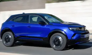Błękitny Opel Mokka z czarnym dachem pędzi po drodze. Sprawdź aktualną opel mokka cena i wybierz swój wymarzony samochód.