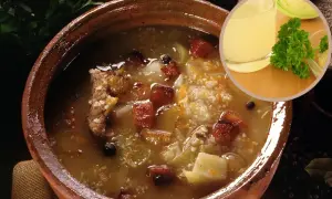 Gęsta zupa z kaszą, mięsem i warzywami w glinianej misce, obok kieliszek bulionu i natka pietruszki.